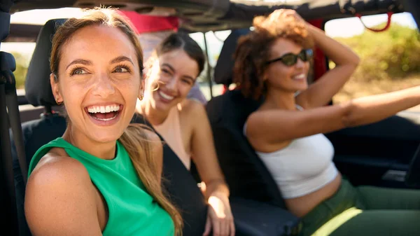 Group Of Laughing Female Friends Having Fun In Open Top Car On Road Trip