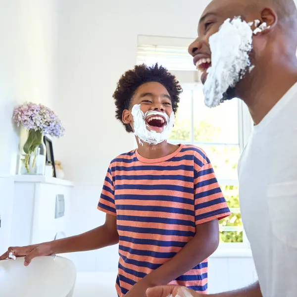 Father And Son At Home Having Fun Playing With Shaving Foam In Bathroom Making A Mess Together