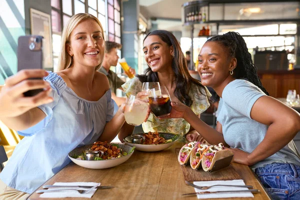 Group Of Female Friends Meeting Up In Restaurant Posing For Selfie On Mobile Phone With Food