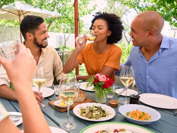 Group Of Friends Enjoying Outdoor Meal And Wine On Visit To Vineyard Restaurant