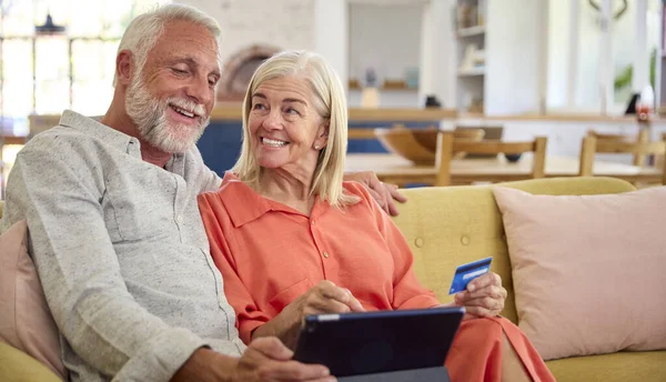 Retired Senior Couple At Home With Digital Tablet Making Purchase Or Booking Using Credit Card