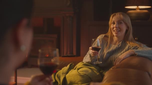Две Подруги Отдыхают Диване Разговаривают Пьют Вино Перед Уютным Камином — стоковое видео