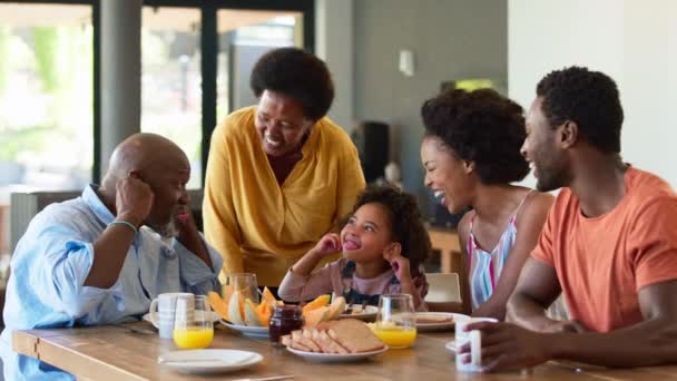 祖父母の両親や孫娘と朝食をとる家族は 自宅のテーブルの周りにメロンを食べて面白い顔を引っ張る スローモーションで撮影 — ストック動画