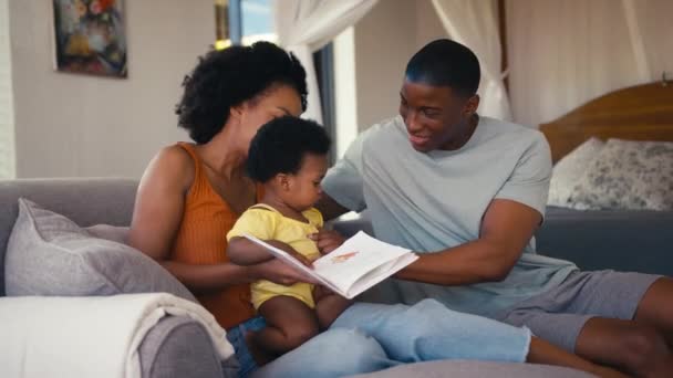 一家人和父母坐在沙发上 带着年幼的女儿看书 动作缓慢 — 图库视频影像