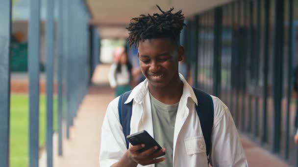 男性の高校生は ソーシャルメディアや携帯電話でインターネットをチェックする教室の外を歩いています スローモーションで撮影 — ストック動画