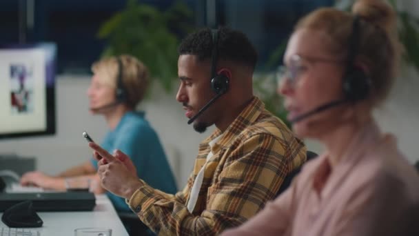 商业团队中头戴耳机 看着手机在客户销售或支持团队中工作到很晚的人 动作缓慢 — 图库视频影像