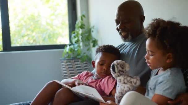Dziadek Siedzi Kanapie Domu Dobrze Się Bawi Czytając Książkę Wnukami — Wideo stockowe