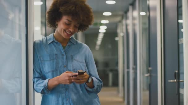 Gülümseyen Genç Kadını Modern Ofiste Duruyor Cep Telefonuyla Mesaj Yazıyor — Stok video
