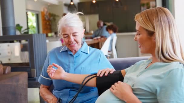 妊娠中の女性を訪問する上級主婦は バックグラウンドで家族と一緒に血圧をチェック スローモーションで撮影 — ストック動画