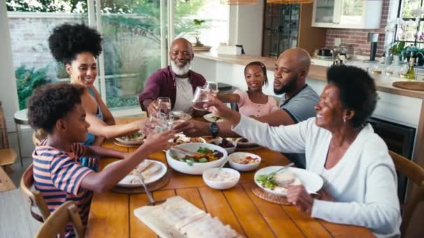 自宅でテーブルの周りに座っている多世代の家族は 食事をする前に水のメガネで応援しています スローモーションで撮影 — ストック動画