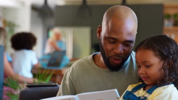 Отец Дочь Читают Книгу Дома Вместе Многодетной Семьей Заднем Плане — стоковое видео