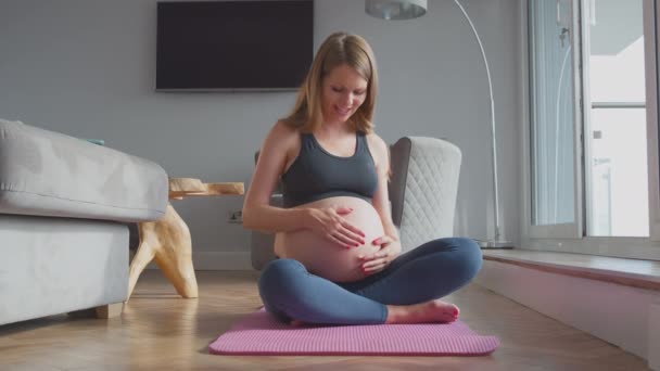 Hamile Kadın Spor Kıyafetleri Içinde Evde Mindere Oturup Karnına Dokunarak — Stok video