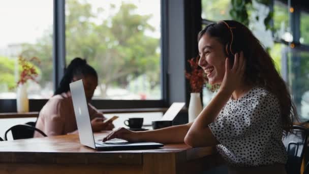 Uśmiechnięta Młoda Bizneswoman Nosząca Słuchawki Bezprzewodowe Siedząca Nieformalnej Części Wypoczynkowej — Wideo stockowe