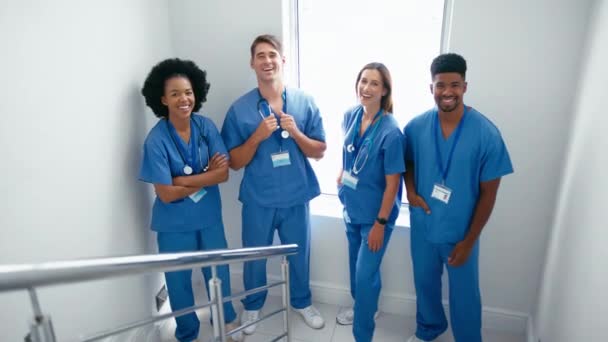 病院の建物内の階段の手すりに傾いているスクラブを着用した多文化医療チームの笑顔の肖像画 ゆっくりとした動きで撮影 — ストック動画