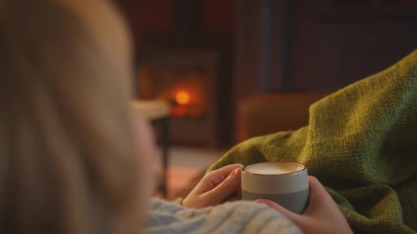 一个女人躺在沙发上 拿着毛毯在家里看着舒适的火堆 喝着热腾腾的饮料 慢镜头 — 图库视频影像