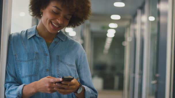 Gülümseyen Genç Kadını Modern Ofiste Duruyor Cep Telefonuyla Mesaj Yazıyor — Stok video
