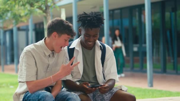 ソーシャルメディアやインターネットを携帯電話でチェックする外壁に座っている2人の男子高校生 スローモーションで撮影 — ストック動画