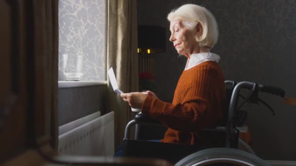 忧心忡忡的老年妇女坐在轮椅上 靠散热器看着家里的能源账单 慢镜头拍摄 — 图库视频影像