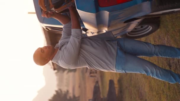 笑顔の男の垂直ビデオ肖像画 バックパックを降ろす サンセットで田舎のキャビンへの道路旅行でトラックをピックアップする スローモーションで撮影 — ストック動画