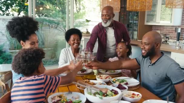 自宅でテーブルの周りに座っている多世代の家族は 食事をする前にワインと水のメガネで応援しています ゆっくりとした動きで撮影 — ストック動画