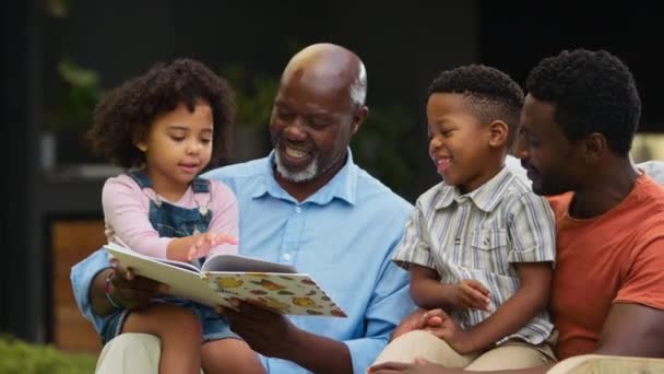 Multi Generational Οικογένεια Κάθεται Στον Κήπο Στο Σπίτι Διασκεδάζοντας Διαβάζοντας — Αρχείο Βίντεο