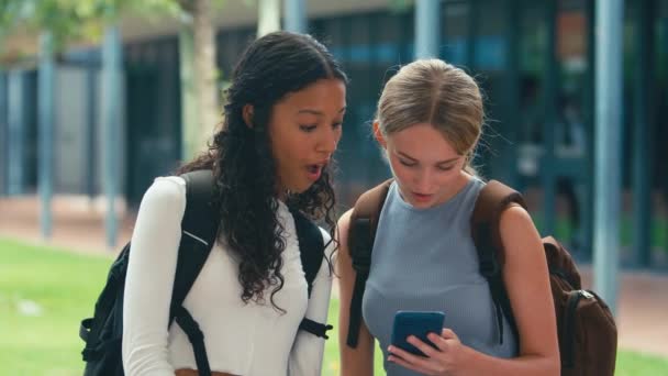 2人の女子高校生が外でソーシャルメディアを携帯電話でチェックし ショックを受けた スローモーションで撮影 — ストック動画