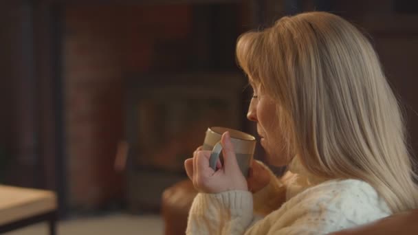 Γυναίκα Κάθεται Στον Καναπέ Στο Σπίτι Μπροστά Από Ζεστή Φωτιά — Αρχείο Βίντεο