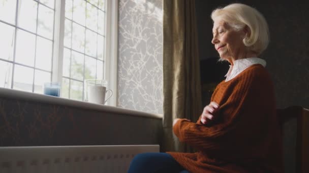 老年妇女在家里坐在散热器旁 试图在能源和生活成本危机期间保暖 喝着热饮 浑身哆嗦 动作缓慢 — 图库视频影像