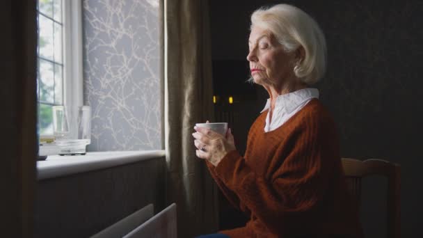 老年妇女在家里坐在散热器旁 试图在能源和生活成本危机期间保暖 喝着热饮 浑身哆嗦 动作缓慢 — 图库视频影像