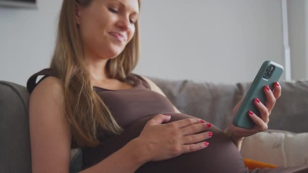 Έγκυος Γυναίκα Χαλαρώνοντας Στον Καναπέ Στο Σπίτι Κοιτάζοντας Κινητό Τηλέφωνο — Αρχείο Βίντεο