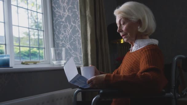 Беспокойная Пожилая Женщина Сидящая Инвалидной Коляске Радиаторе Дома Глядя Счета — стоковое видео