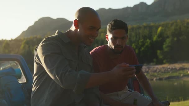 两名男性朋友坐在卡车的尾门上 一边在路上喝啤酒 一边观看运动在手机上慢镜头 — 图库视频影像