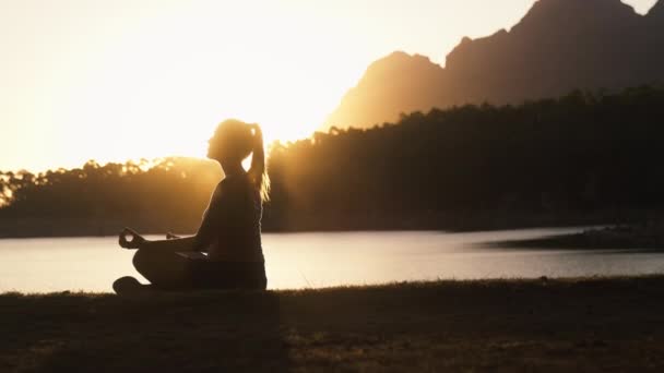 Силуэт Женщины Расслабляющей Сидя Красивого Озера Гор Закате Делая Йогу — стоковое видео