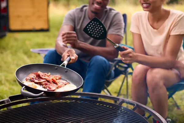 Close Up Of Couple Camping In Countryside With RV Cooking Bacon And Eggs For Breakfast On Fire