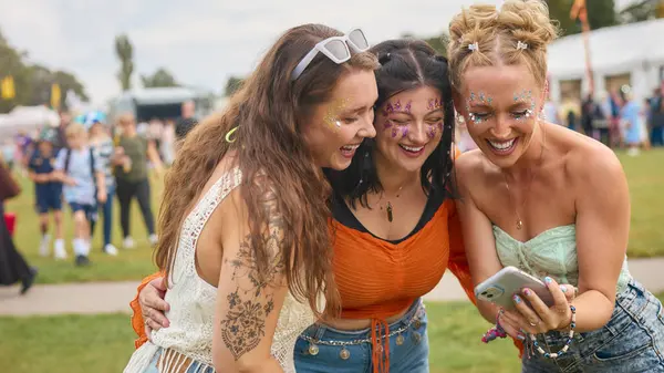 Trzy Przyjaciółki Noszące Brokat Patrzące Telefon Komórkowy Letnim Festiwalu Muzycznym Zdjęcia Stockowe bez tantiem