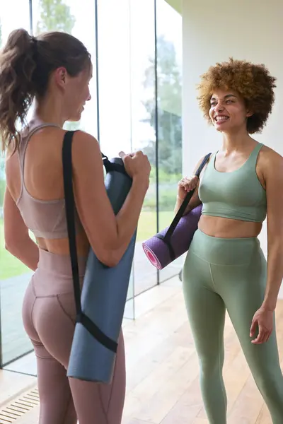 Two Female Friends Wearing Gym Clothing Meeting At Gym Or Yoga Studio For Exercise