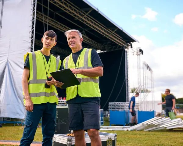 Male Production Team With Flight Cases Setting Up Outdoor Stage For Music Festival