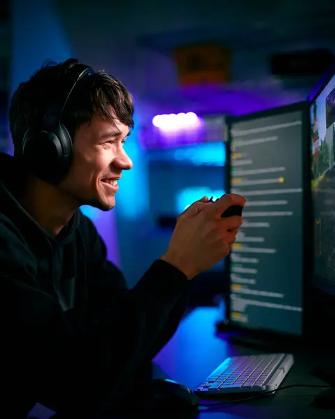 ヘッドホンおよびコントローラーが付いているコンピュータ スクリーンの前の男性のゲーマーの低いキーの照明ショット — ストック写真