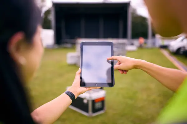 Close Up Of Production Team Looking At Digital Tablet Setting Up Outdoor Stage For Music Festival