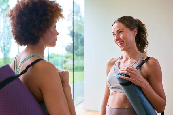 Two Female Friends Wearing Gym Clothing Meeting At Gym Or Yoga Studio For Exercise