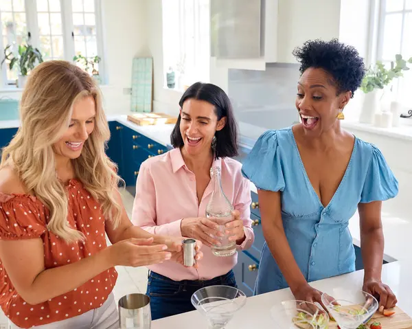 Three Mature Female Friends At Home Having Fun Mixing Cocktails Together