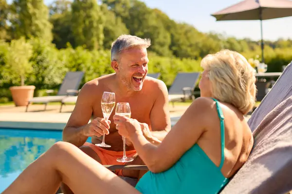 Senior Couple On Holiday In Swimming Costumes Drinking Champagne By Hotel Swimming Pool