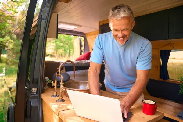 老年人在乡间露营旅行用手提电脑在房车内工作 — 图库照片