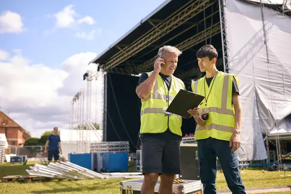 Production Team Talking On Radios And Setting Up Outdoor Stage For Music Concert Or Festival