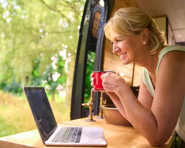 Senior Woman On Camping Trip In Countryside Working Inside RV Using Laptop