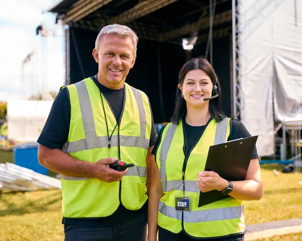 Portrait Of Production Team With Headsets Setting Up Outdoor Stage For Music Festival Or Concert