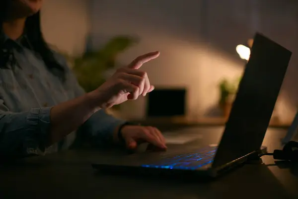 夜间用手提电脑与手指伸出手触摸屏幕的女性的近视 图库图片