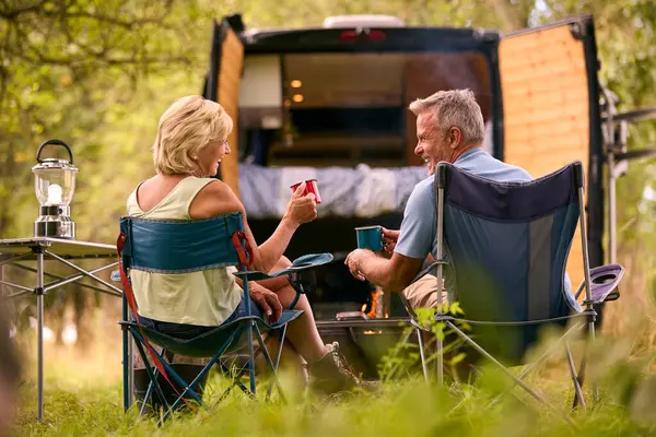 户外篝火边喝咖啡的农村老年夫妇露营背景图 图库图片