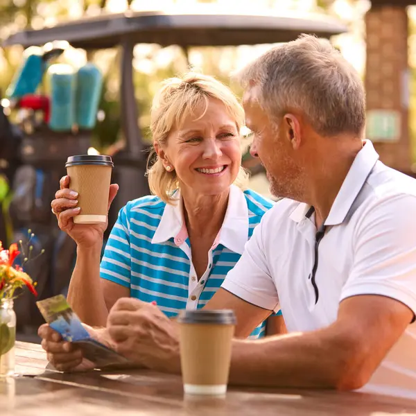 Seniorpaar Sitzt Nach Golfrunde Beim Kaffee Und Schaut Sich Gemeinsam Stockbild