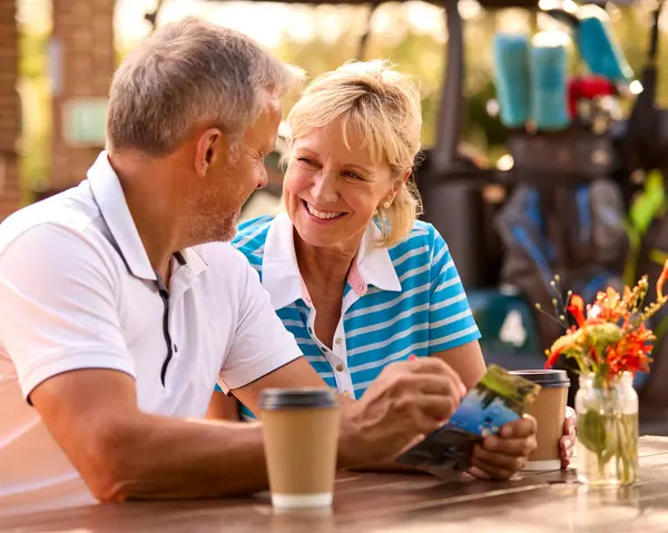 Seniorpaar Sitzt Nach Golfrunde Beim Kaffee Und Schaut Sich Gemeinsam Stockfoto